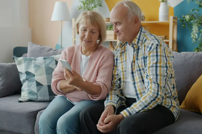 An older couple looking at a smartphone together on their couch
